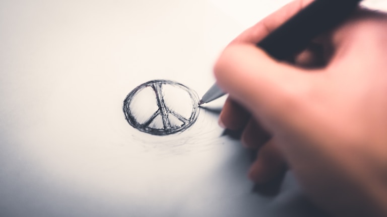A close-up of a hand sketching a logo design with a pencil on textured paper.