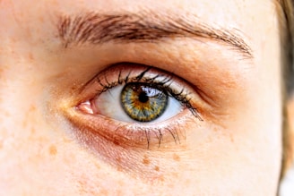 A close-up view of a human eye showcasing intricate details of the iris, eyelashes, and surrounding skin textures. The iris displays a mix of blue and brown colors, creating a striking appearance.