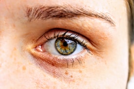 A close-up view of a human eye showcasing intricate details of the iris, eyelashes, and surrounding skin textures. The iris displays a mix of blue and brown colors, creating a striking appearance.