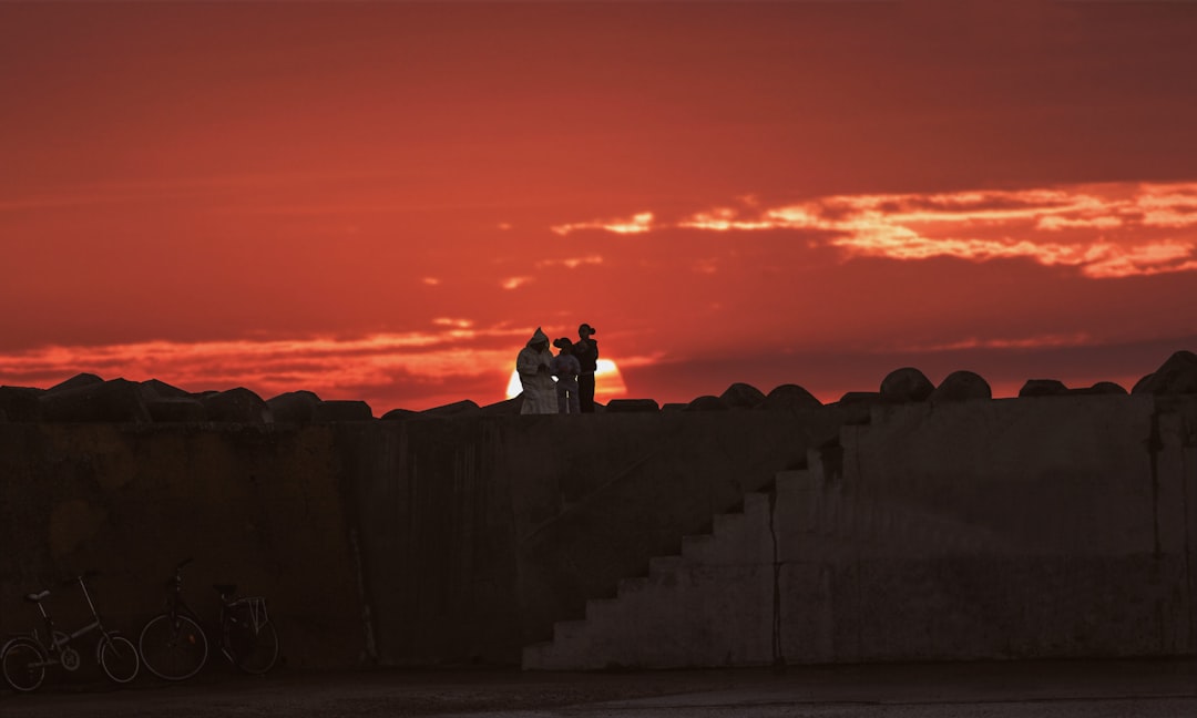 silhouette of man and woman sitting on concrete wall during sunset