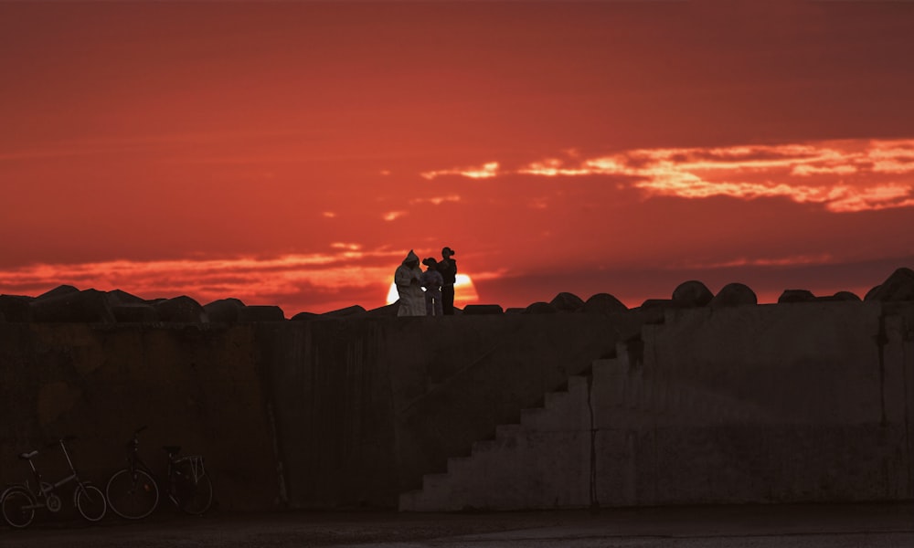 silhueta do homem e da mulher sentados na parede de concreto durante o pôr do sol