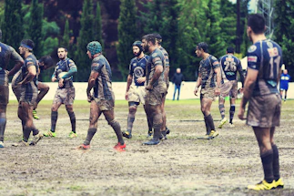 A diverse group of young rugby players smiling together on a sunny field.