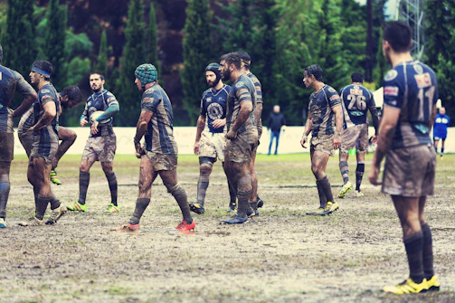 A diverse group of young rugby players smiling together on a sunny field.