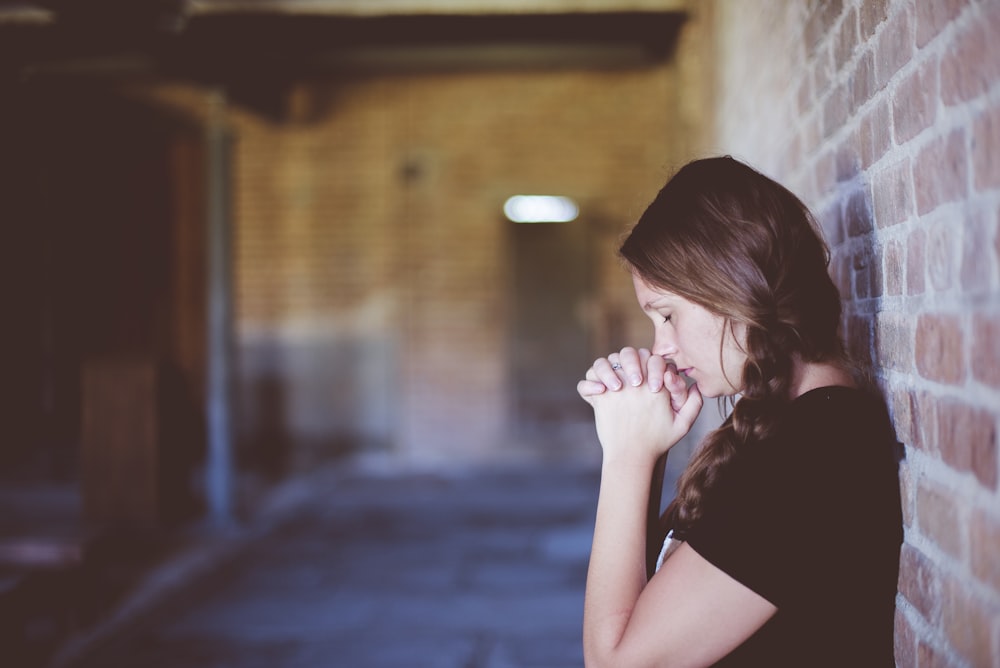Mujer rezando mientras se apoya contra la pared de ladrillo