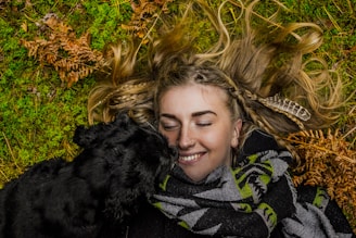 smiling woman lying on ground beside black dog at daytime