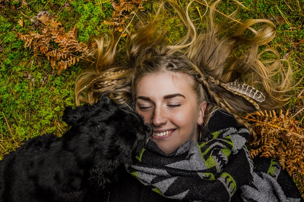 smiling woman lying on ground beside black dog at daytime