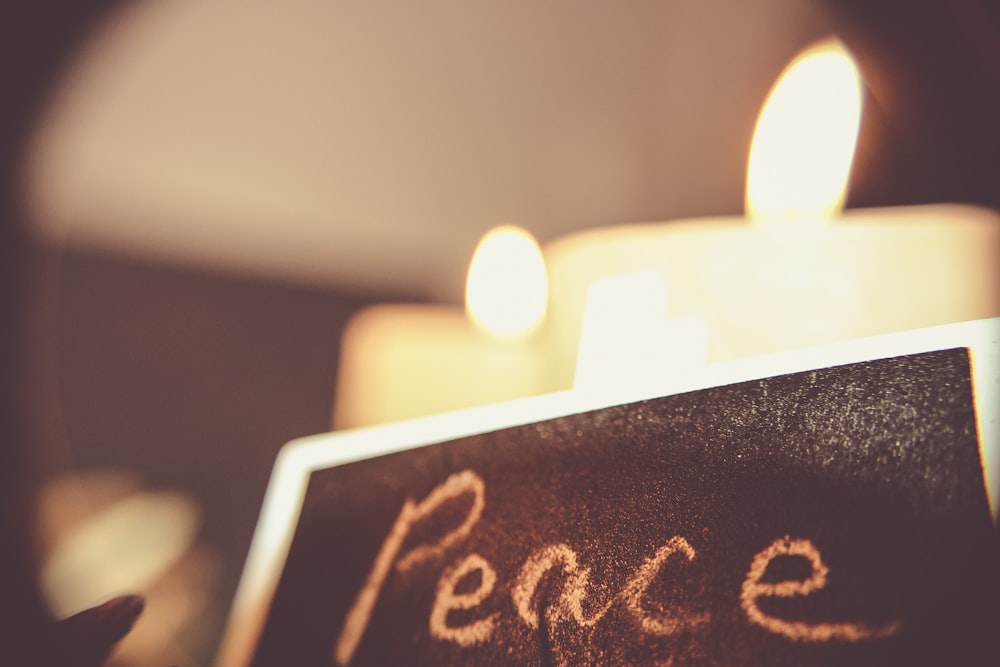 Peace, written on a black chalkboard with white chalk in front of candles.