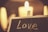 A soft-focus image with the word 'Love' written on a chalkboard in front of a warm, glowing candle. The ambiance is cozy and intimate, with the flickering light casting a gentle glow.