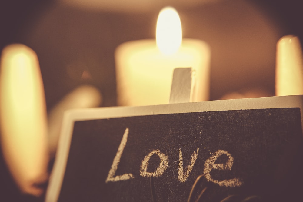 A black chalkboard that says "Love," with white candles in the background.