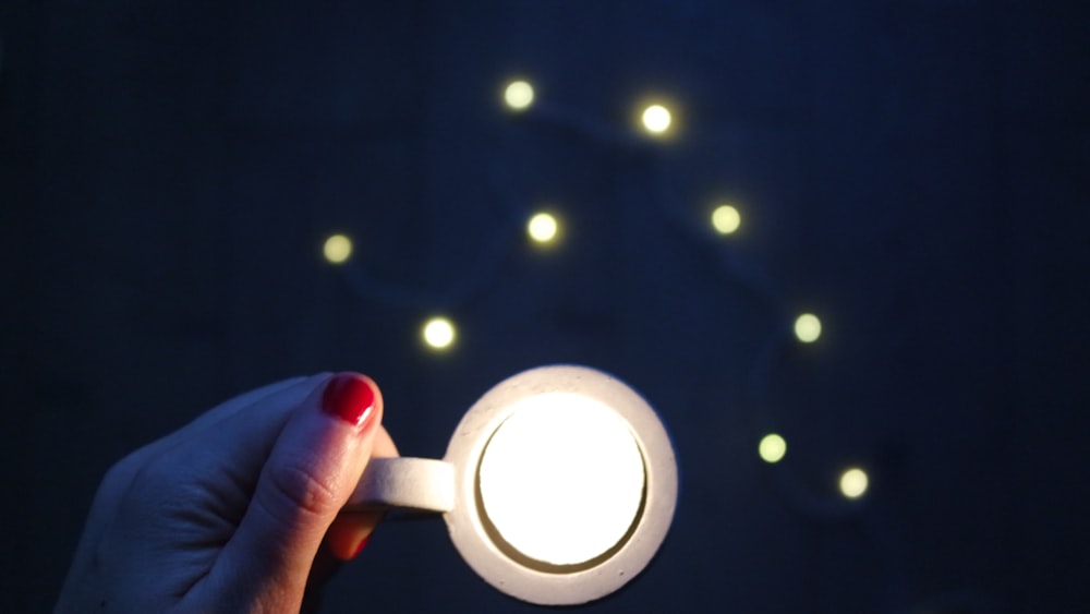 A woman with red fingernail polish holding a cup with a white light in it.