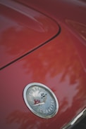 A close-up view of a red car's hood featuring the Chevrolet Corvette emblem, which includes the brand’s iconic crossed flags badge.