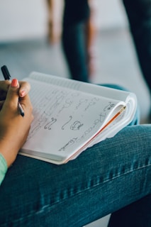 A person writing notes in a notebook surrounded by sketches.
