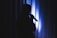 A silhouetted figure is holding a microphone against a backdrop of vertical blue-lit curtains, creating a dramatic and contemplative ambiance.
