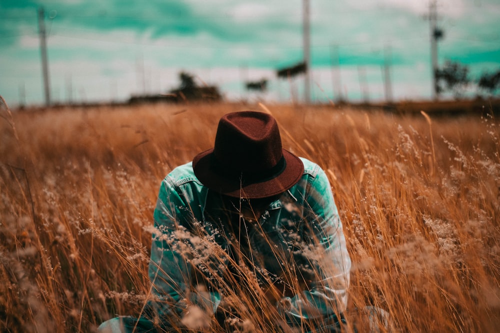 man squatting surrounded by brown grass during daytime