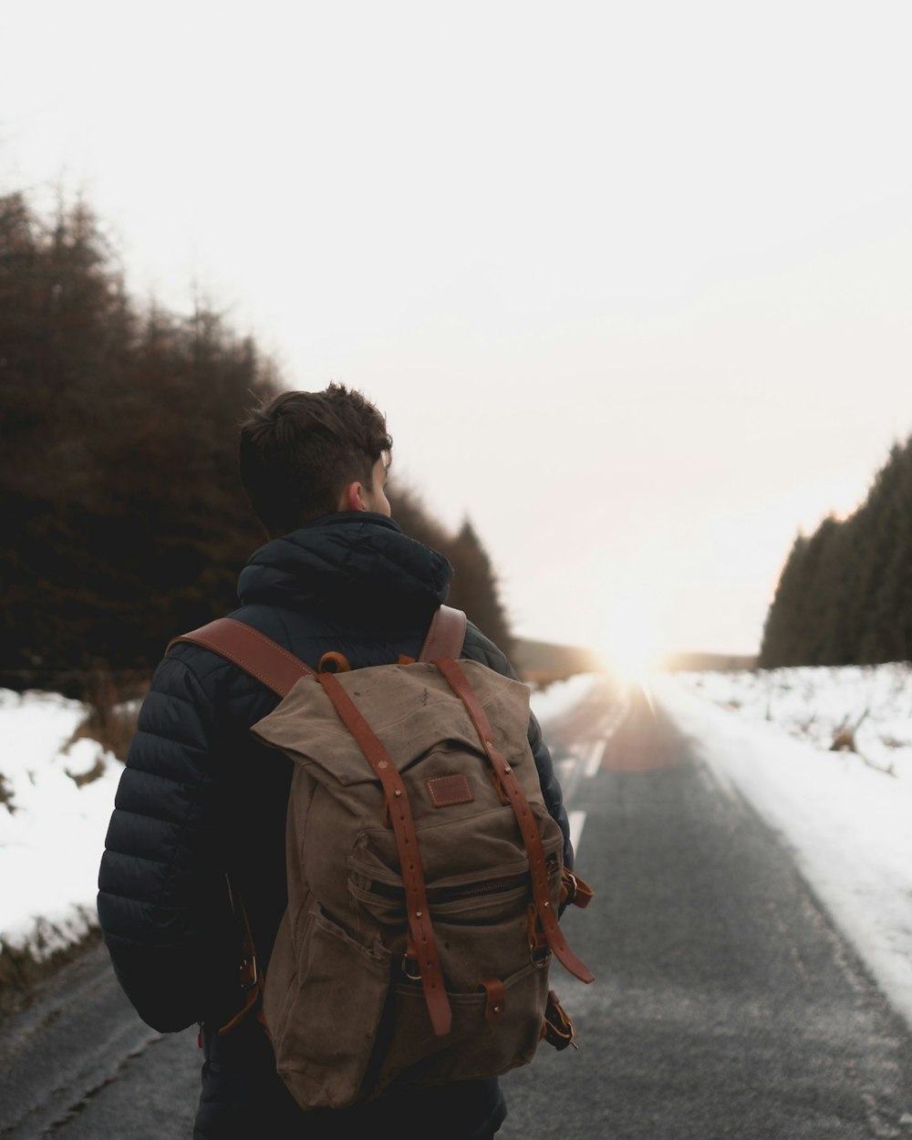 man with backpack standing in middle of road at daytime