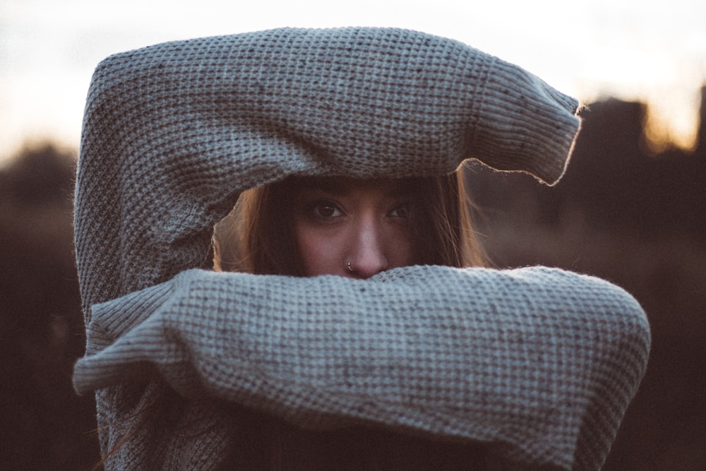 Young woman in a sweater shields forehead and mouth with forearms