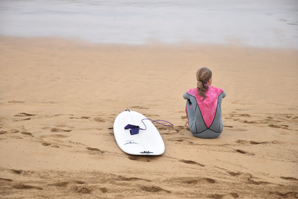 woman sitting on shore beside surfboard near sea