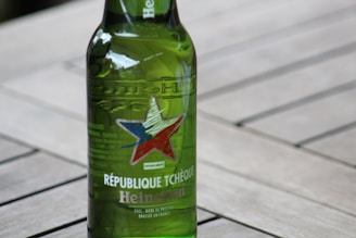 A green Heineken beer bottle with a star design and text indicating 'République Tchèque', placed on a wooden surface.
