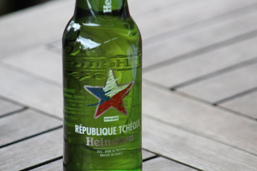 A green Heineken beer bottle with a star design and text indicating 'République Tchèque', placed on a wooden surface.