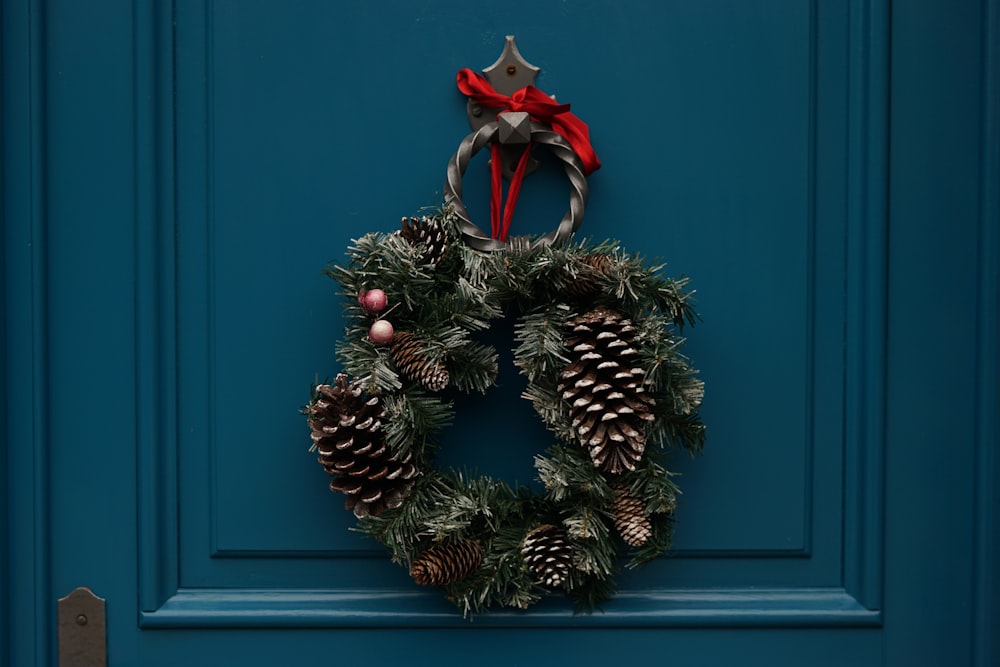 An evergreen wreath decorated with berries and pine cones hangs on a teal door