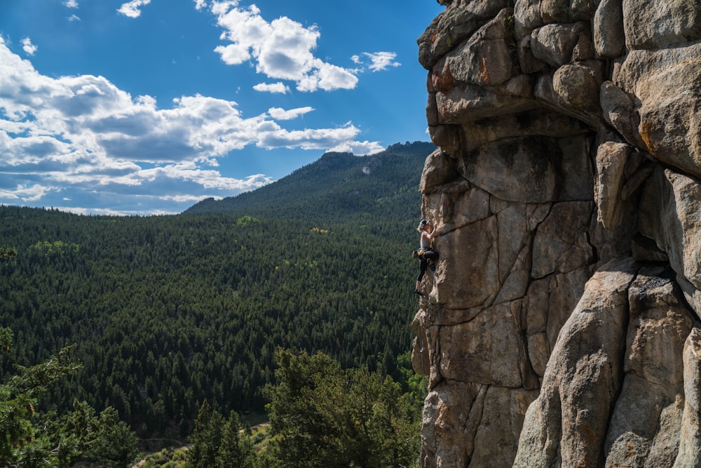 person doing rock climbing under white clouds at daytime