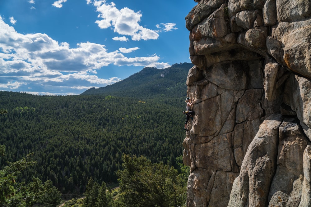 Persona que hace escalada en roca bajo nubes blancas durante el día