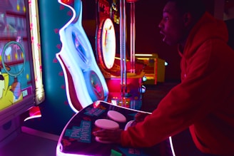 A group of friends intensely playing arcade machines under neon red and pink lights.