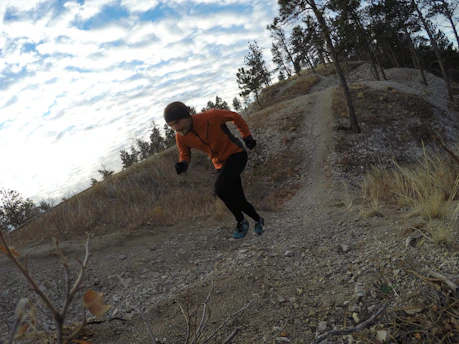 A trail runner crossing a rocky mountain path at sunrise with vibrant orange and red hues in the sky.
