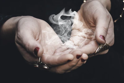 Close-up of a hand holding a vintage tarot card with smoke swirling around it.