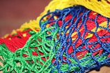 A vibrant collection of intertwined plastic ropes in various colors, including bright red, green, blue, and yellow, forming a complex, mesh-like pattern.