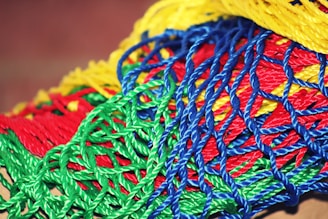 A vibrant collection of intertwined plastic ropes in various colors, including bright red, green, blue, and yellow, forming a complex, mesh-like pattern.