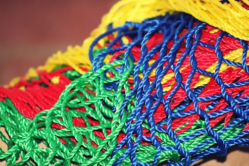 A vibrant collection of intertwined plastic ropes in various colors, including bright red, green, blue, and yellow, forming a complex, mesh-like pattern.
