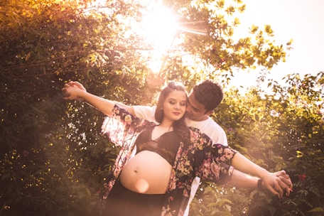A joyful couple embracing outdoors, holding a positive pregnancy test with sunlight filtering through trees.