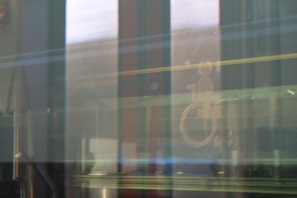 A blurred view through a reflective glass window showing faint outlines of structures outside, with a wheelchair accessibility symbol visible on the glass.
