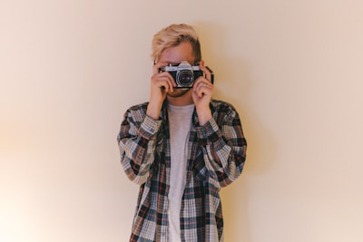 man wearing black, gray, and brown plaid collared button-up long-sleeved shirt standing while using camera