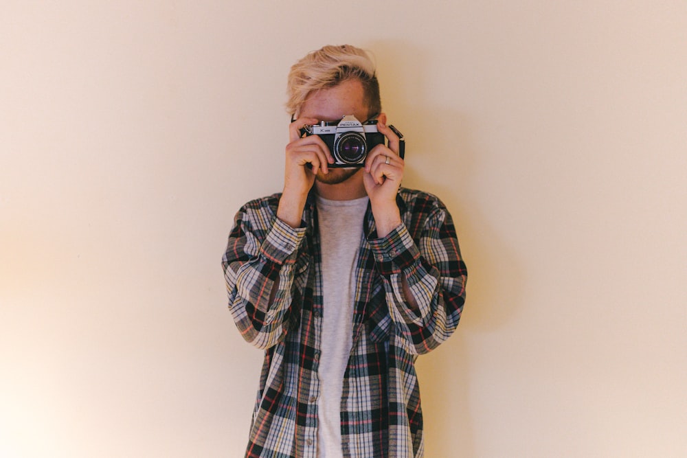 man wearing black, gray, and brown plaid collared button-up long-sleeved shirt standing while using camera