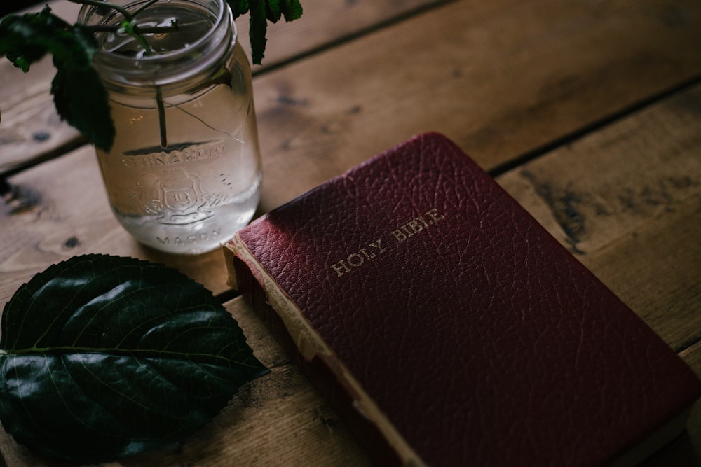 Holy Bible beside clear mason jar on table