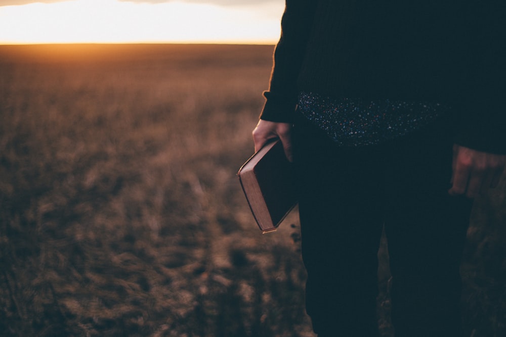 person holding book while standing on field