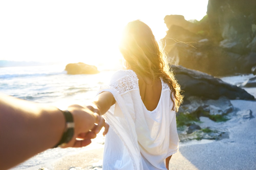 太陽の光を浴びながら海辺で女性の手を握る人