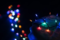 Colorful lights are arranged on a dark surface, creating a festive and vibrant contrast. On the right side, several small LED bulbs emit bright colors, including red, blue, green, and orange. In the background, bokeh effects showcase blurred multicolored lights.