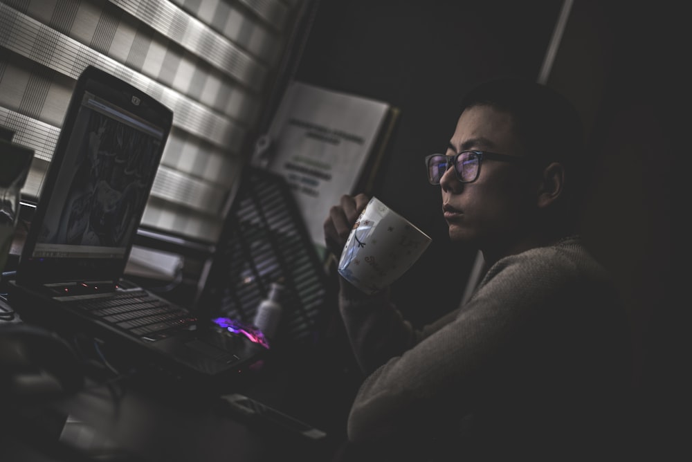 homem segurando caneca na frente computador portátil