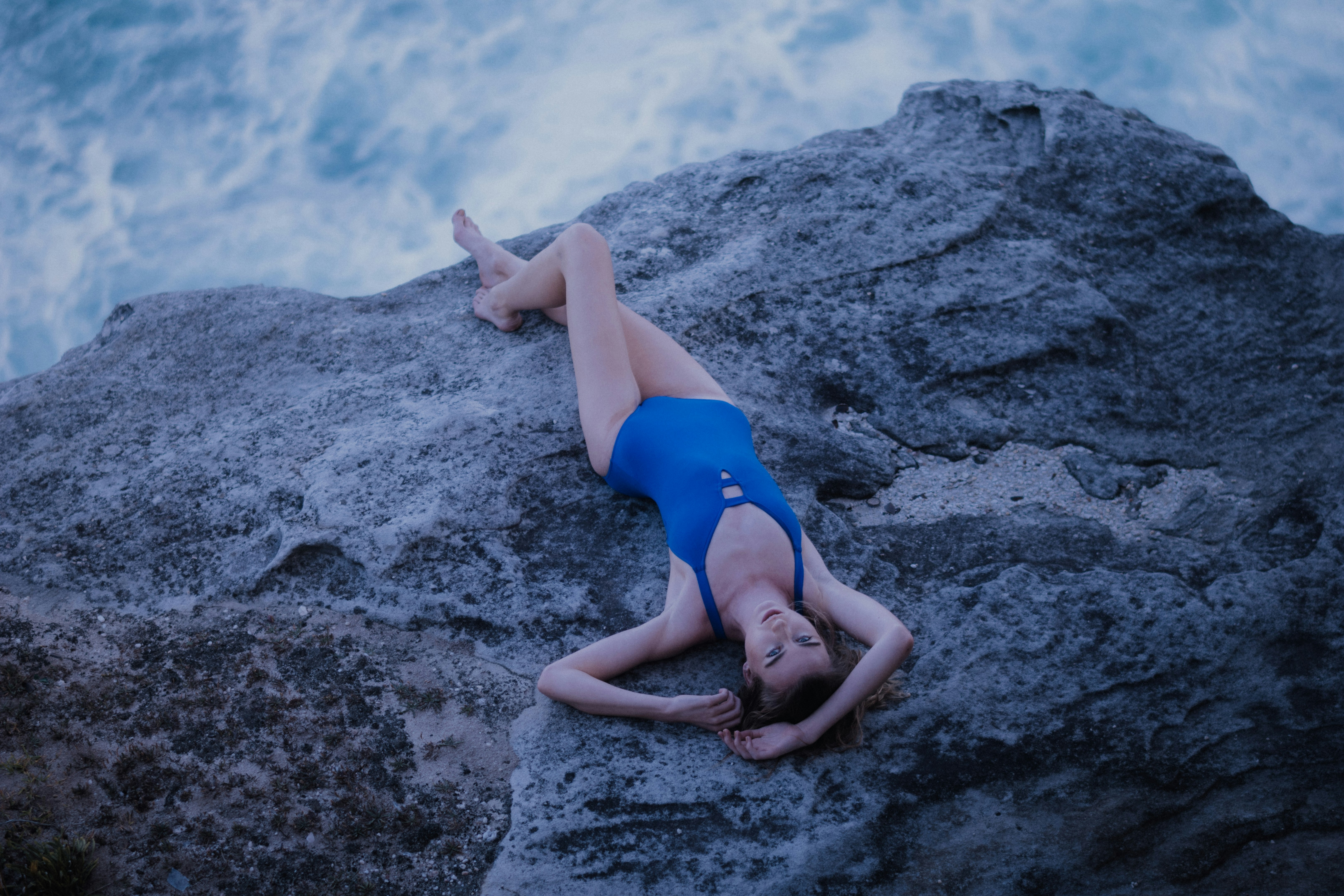 woman lying on boulder neat water