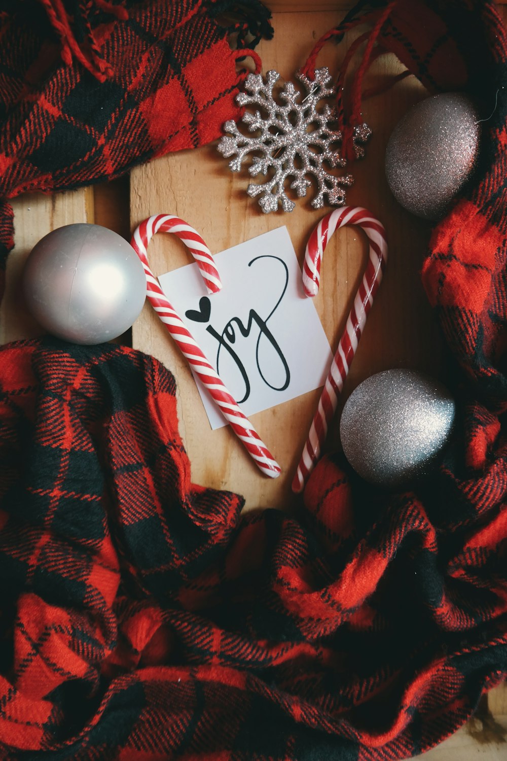 Una nota blanca que dice "Alegría", rodeada de bastones de caramelo, adornos navideños y tela escocesa roja.