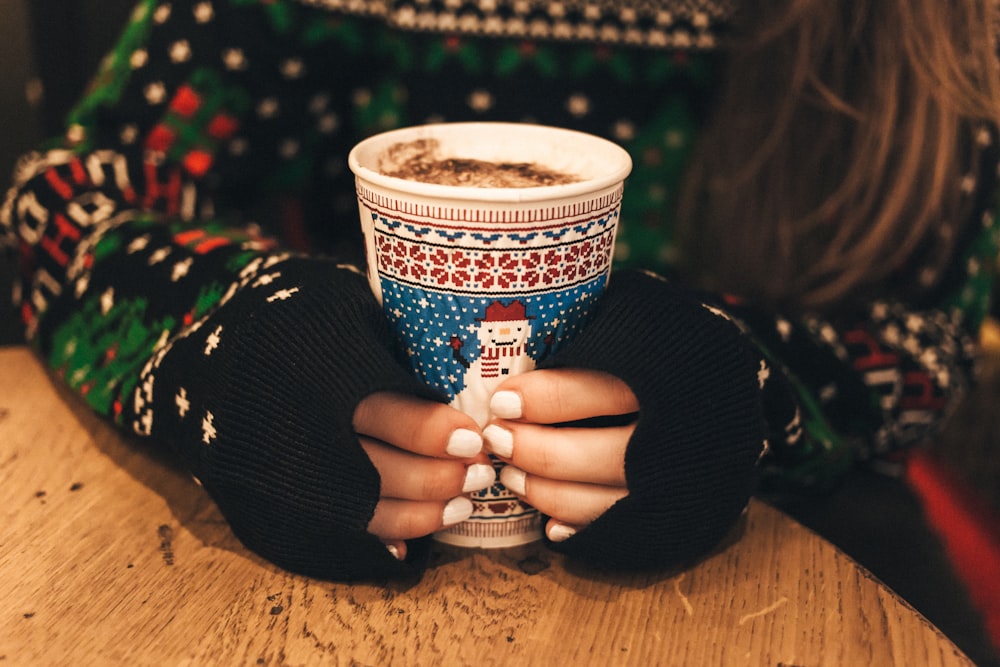 Eine langhaarige Frau mit weiß lackierten Nägeln hält eine Tasse heiße Schokolade in der Hand.