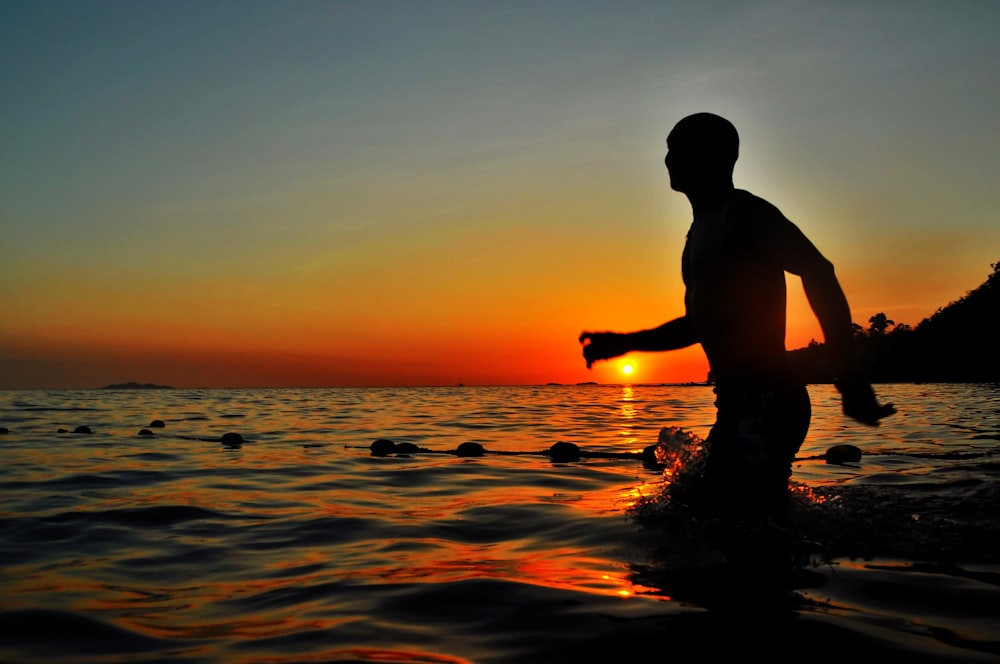 silhouette of man walking in body of water