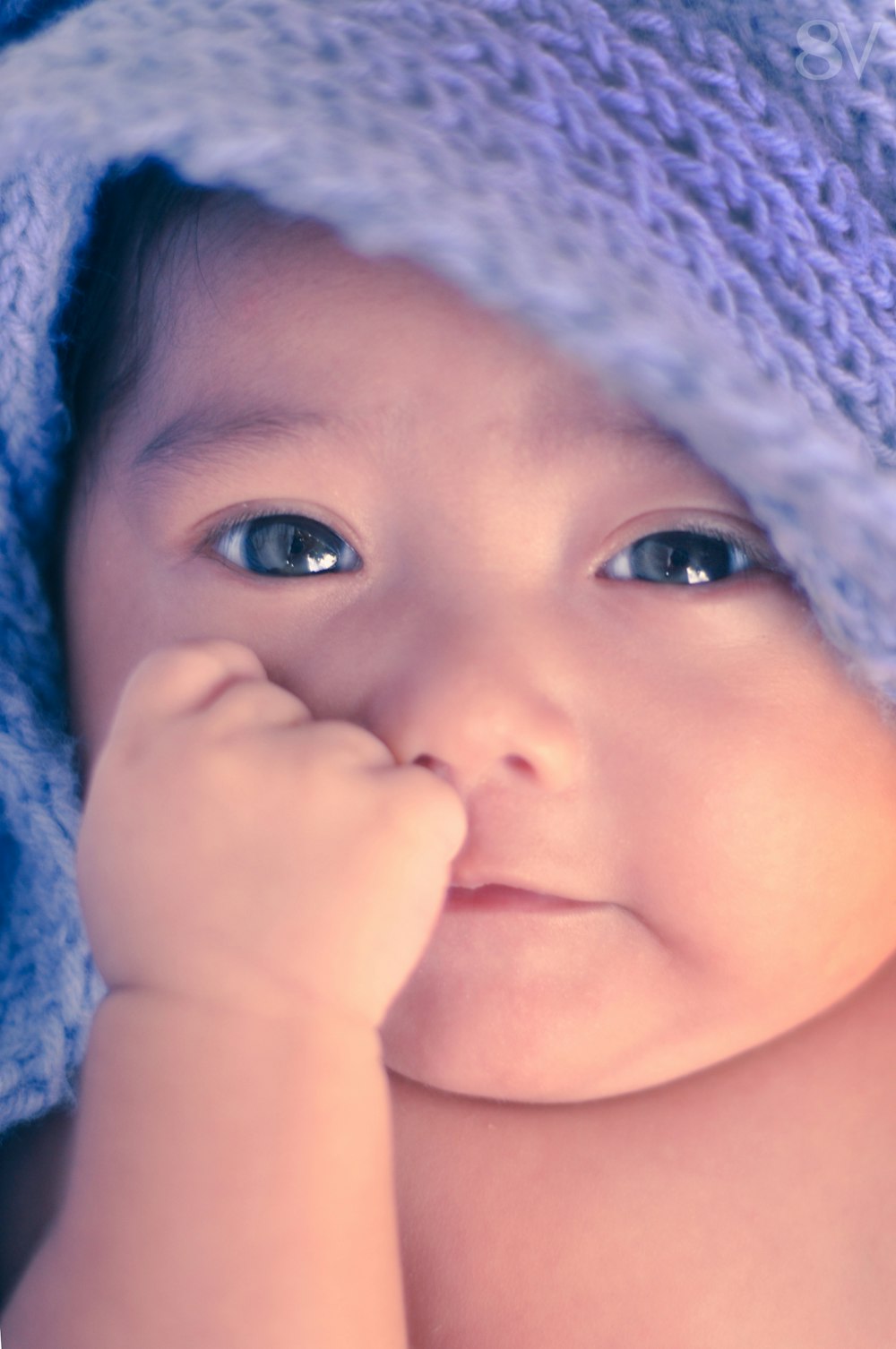 Un bebé feliz con una manta sobre la cabeza.