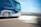 A moving coach bus captured in motion blur, creating a dynamic and fast-paced effect. The bus is predominantly blue and white, featuring a logo and text on its side. The background shows a road and sky blurred due to the motion.