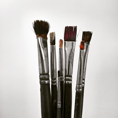 A collection of paintbrushes with metallic handles and bristles of various lengths and shapes, standing upright against a plain background.