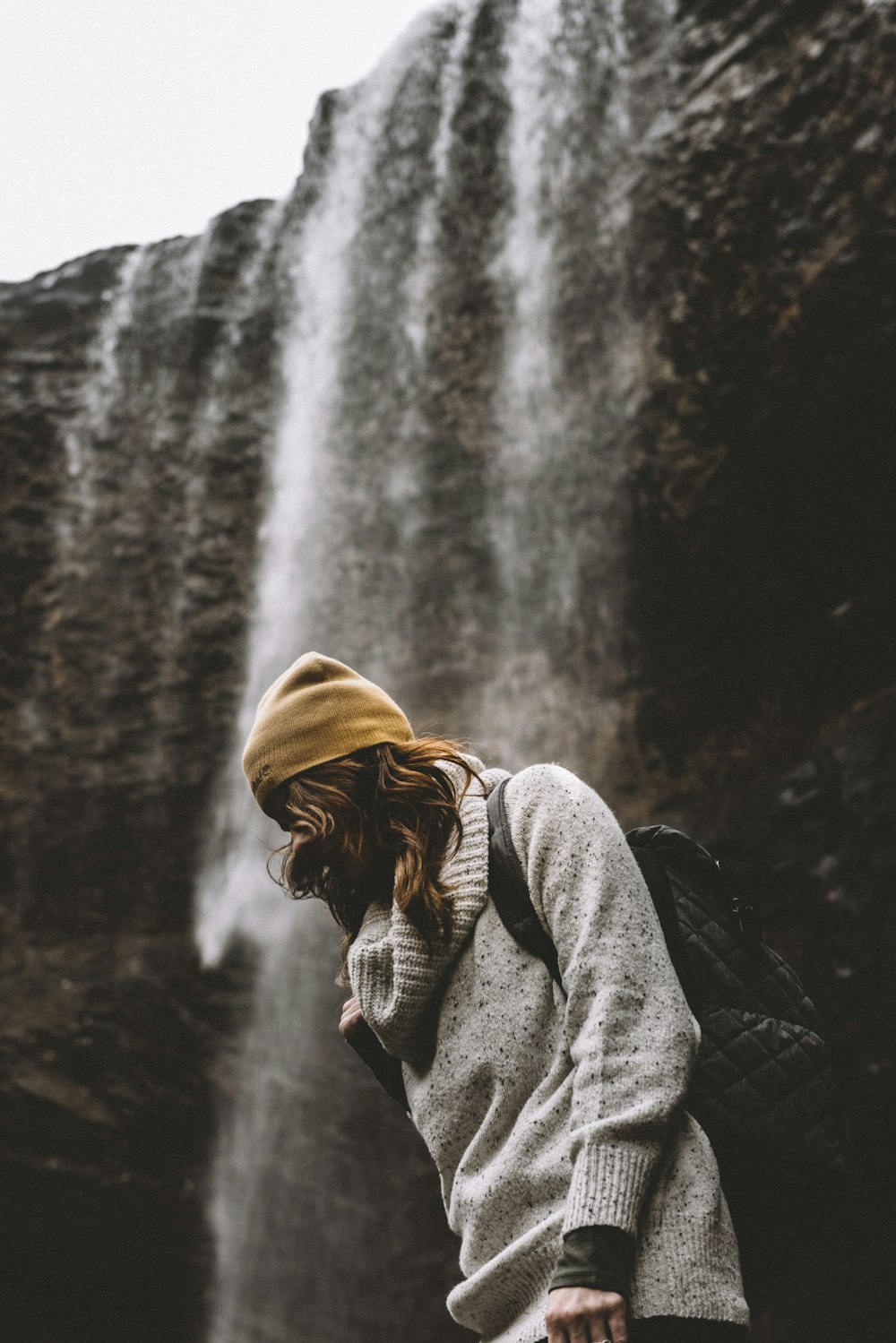 woman in knit cap standing near waterfalls