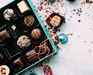 A hand delivering a beautifully wrapped box of chocolates on a cobblestone street.